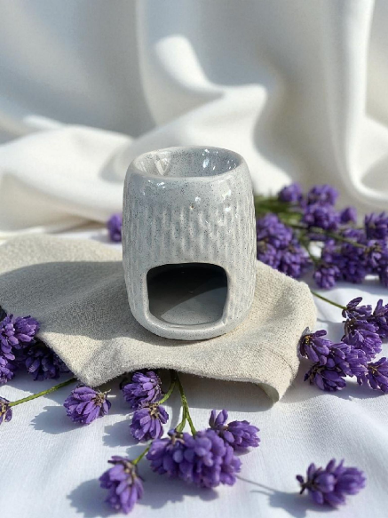 Un difusor de aceite de cerámica gris claro con ramitas de lavanda sobre un fondo de tela blanca.