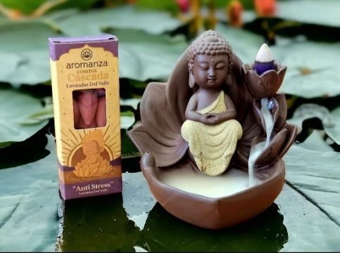 Un quemador de incienso de Buda con humo cayendo en cascada, junto a una caja de conos de incienso de lavanda.