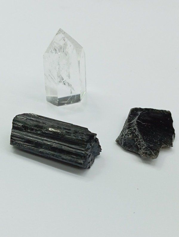 Punta de cristal de cuarzo transparente con dos piezas de turmalina negra sobre fondo blanco.