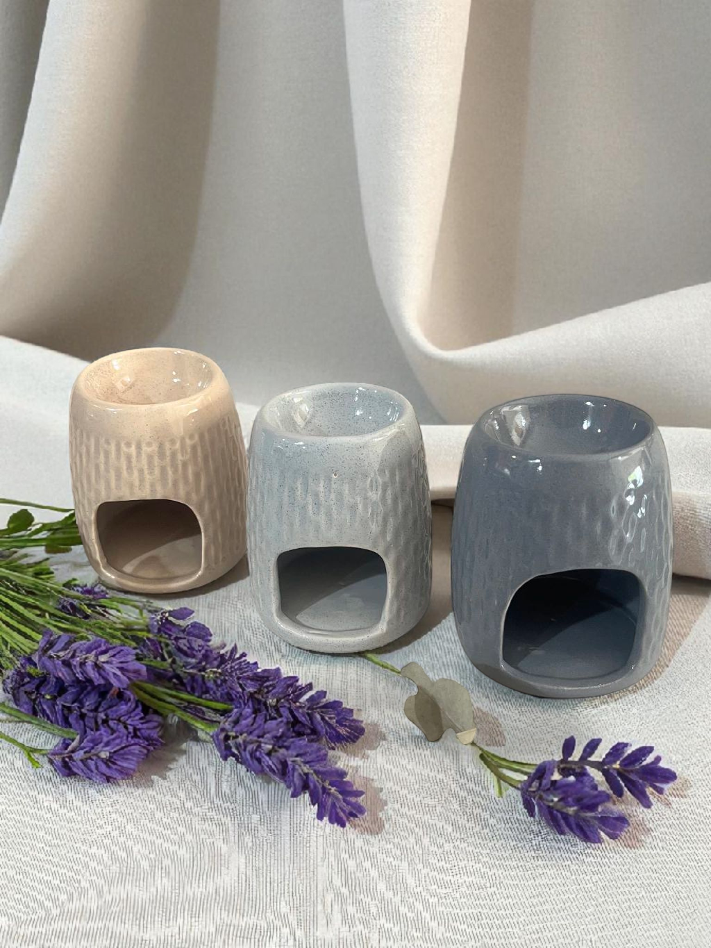 Difusor de aceites esenciales de cerámica gris con lavanda sobre tela blanca de fondo.