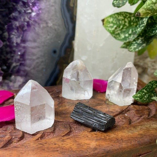 Tres cristales de cuarzo transparente y una turmalina negra sobre una superficie de madera, con un cristal púrpura al fondo.