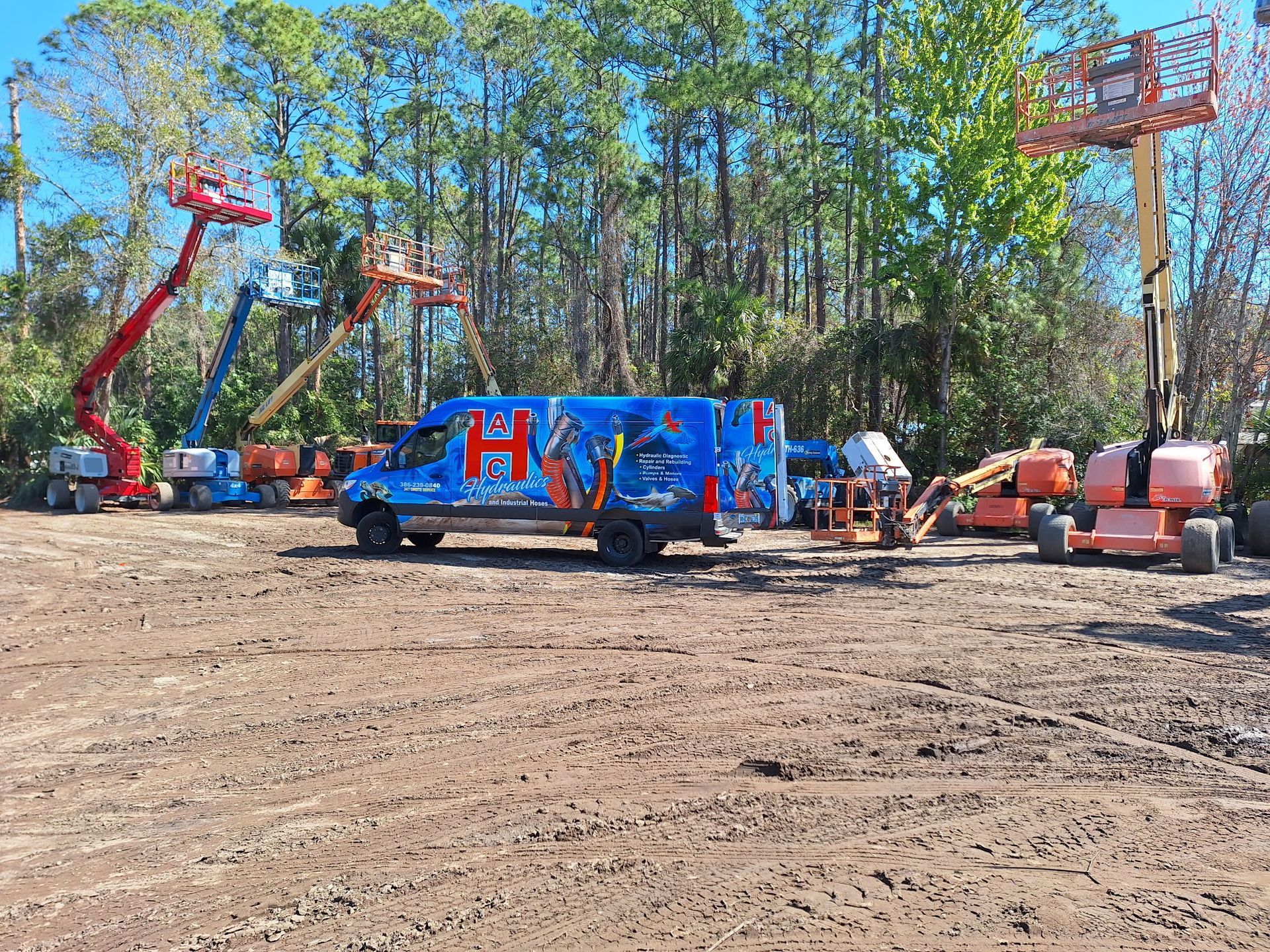 A blue On-Site Hydraulic Hose Repair Van is parked in a dirt field next to a row of man lifts.