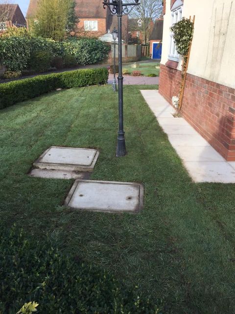 Patch of grass at side of house with tall lamps and paving slabs