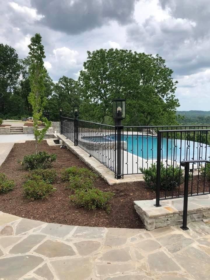 A fence surrounds a swimming pool with trees in the background