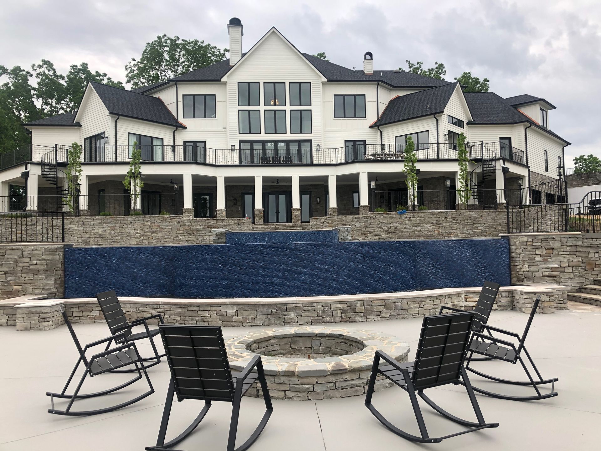 A large house with a fire pit and rocking chairs in front of it.