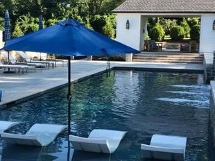 A large swimming pool with a blue umbrella and white chairs