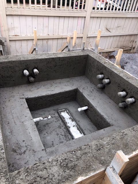 A concrete bathtub is being built in a backyard.