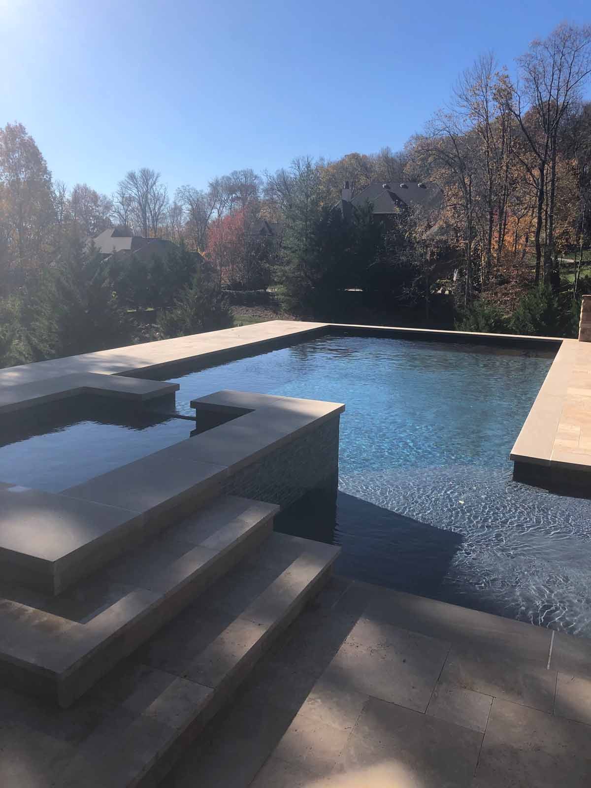 A large swimming pool with stairs leading to it and trees in the background.