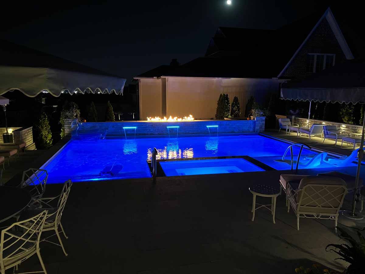 A large swimming pool is lit up at night with blue lights.