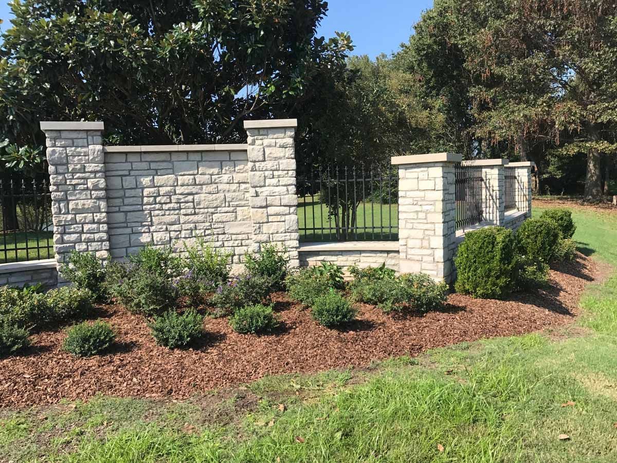 A stone wall with a gate and bushes in front of it