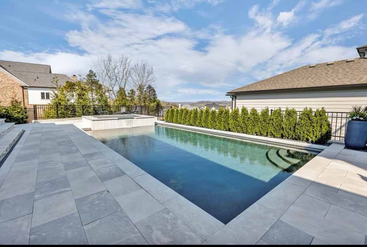 A large swimming pool is in the backyard of a house.