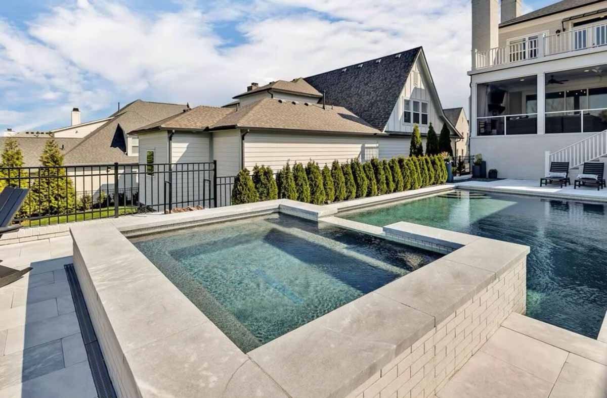 A large swimming pool with a hot tub in front of a house.