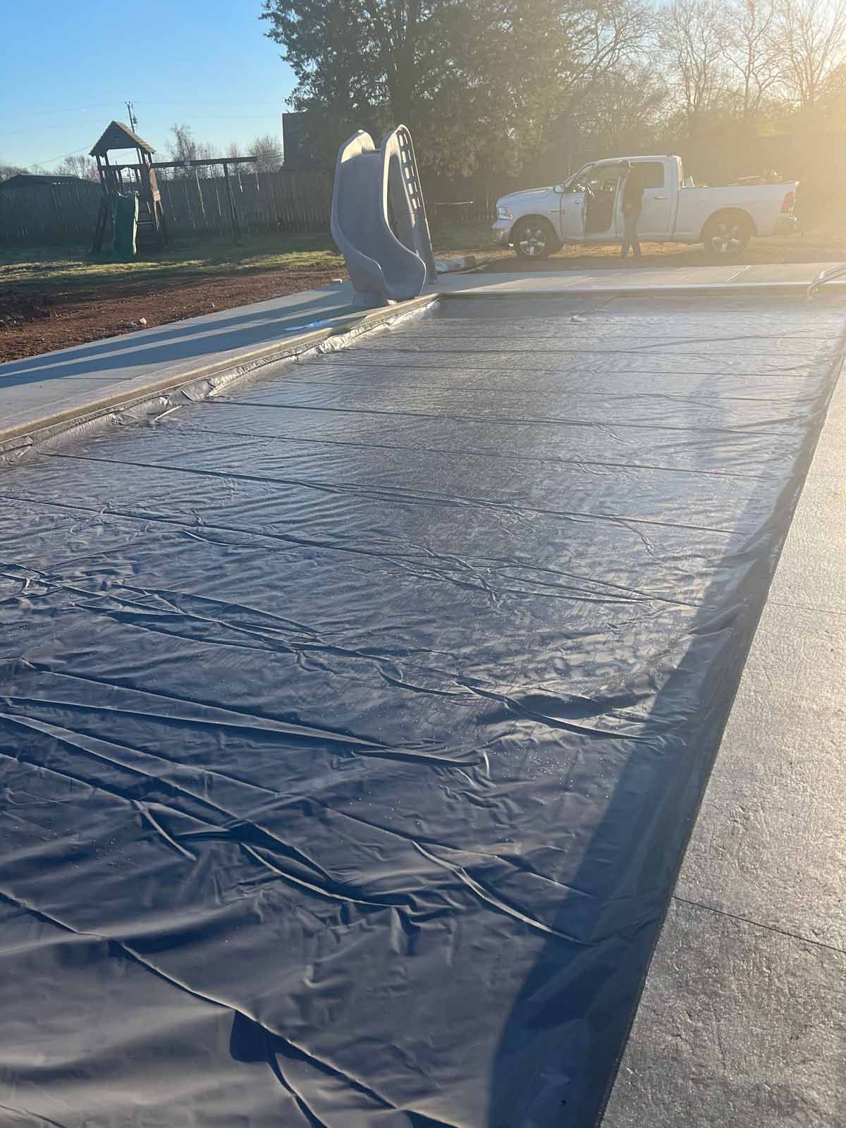 A white truck is parked on the side of the road next to a black tarp.