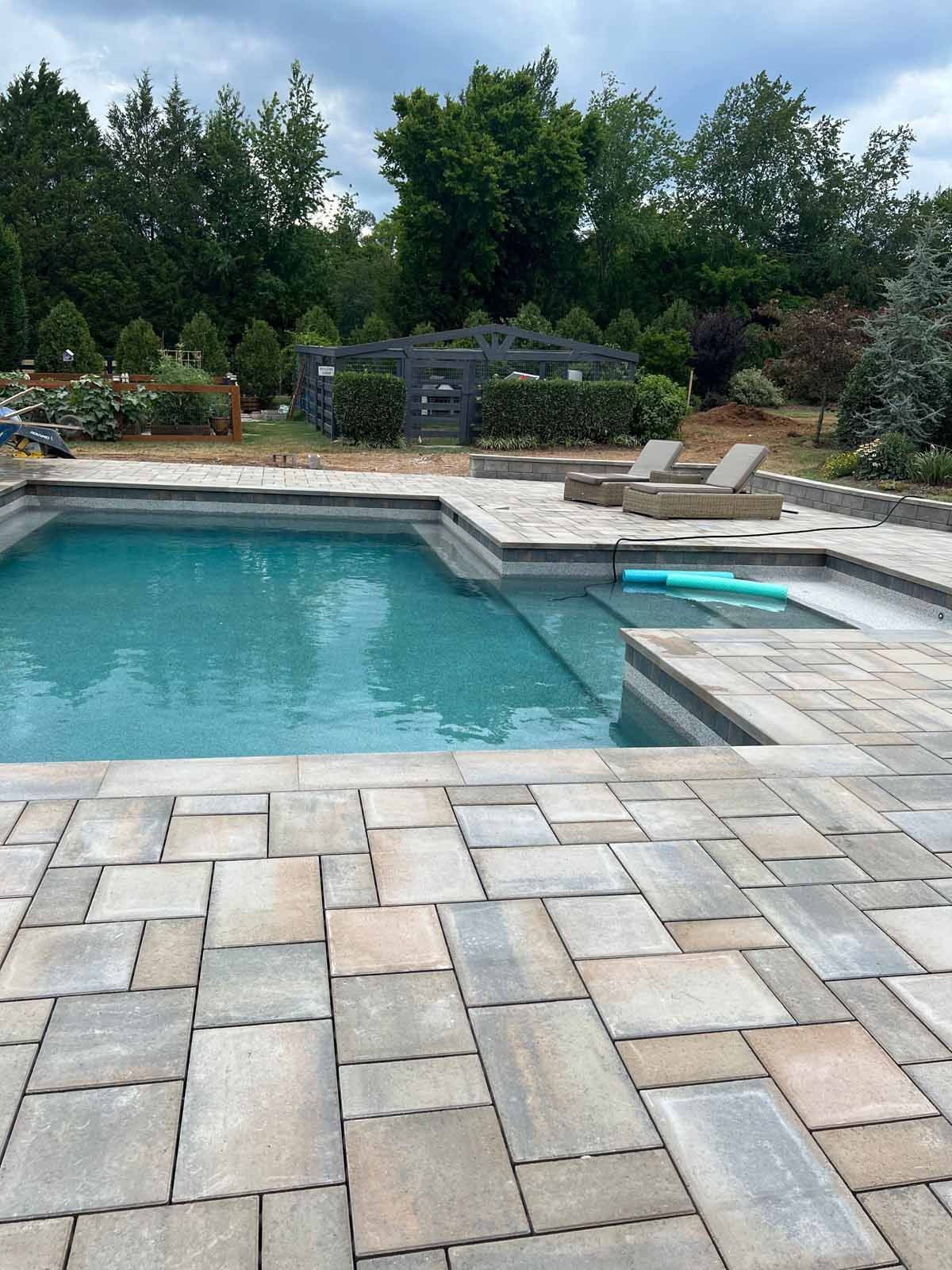 A large swimming pool is surrounded by a brick patio.