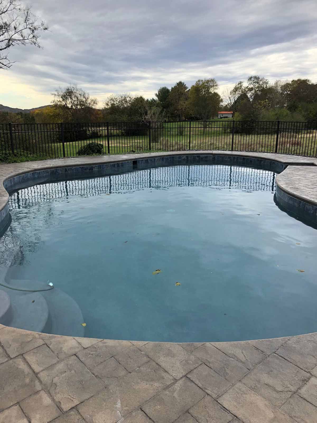 A large swimming pool with a fence around it and trees in the background.