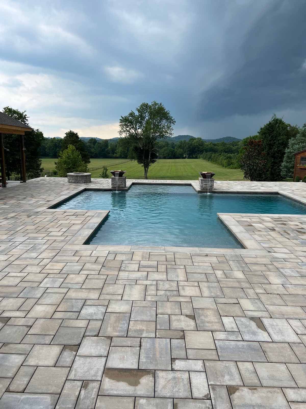 A large swimming pool is surrounded by a brick patio.