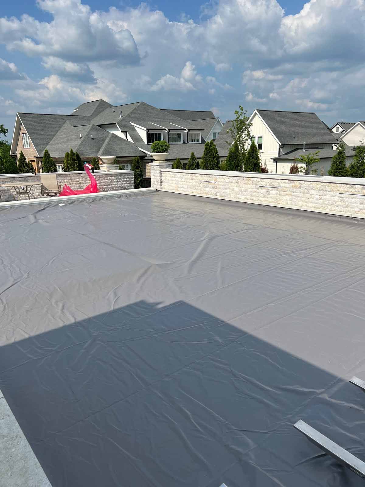 A roof with a tarp on it and houses in the background.