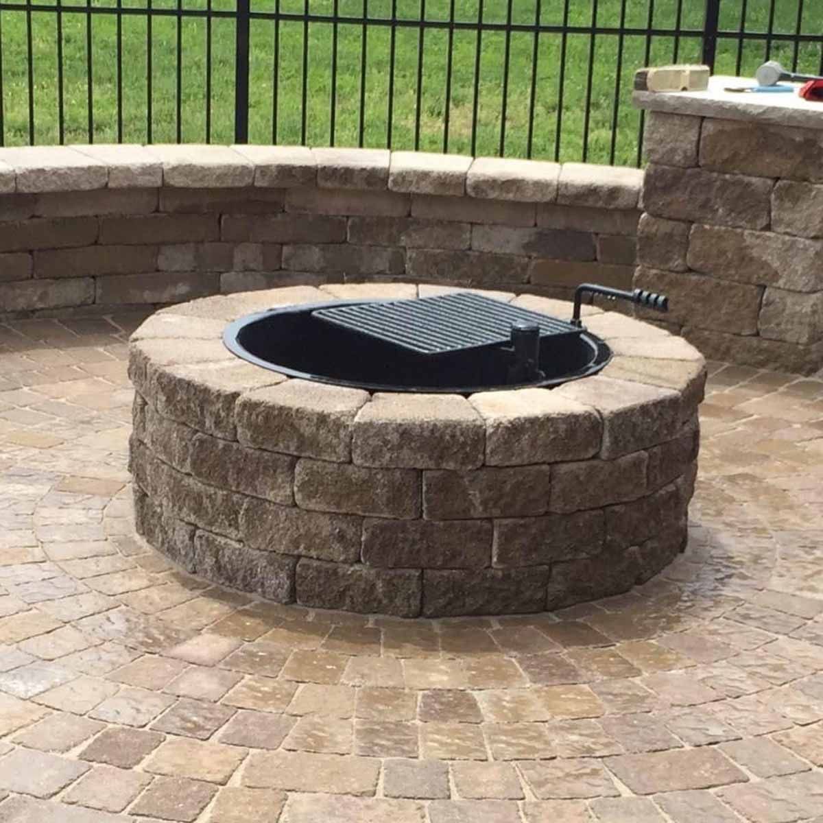 A fire pit is sitting on a brick patio next to a fence.