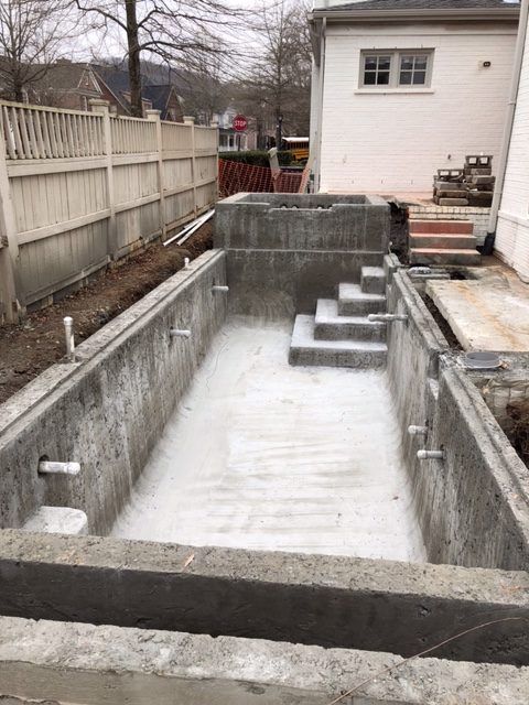 A large concrete pool is being built in the backyard of a house.