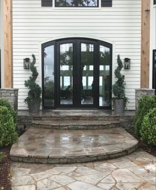 A white house with black doors and a stone patio in front of it.