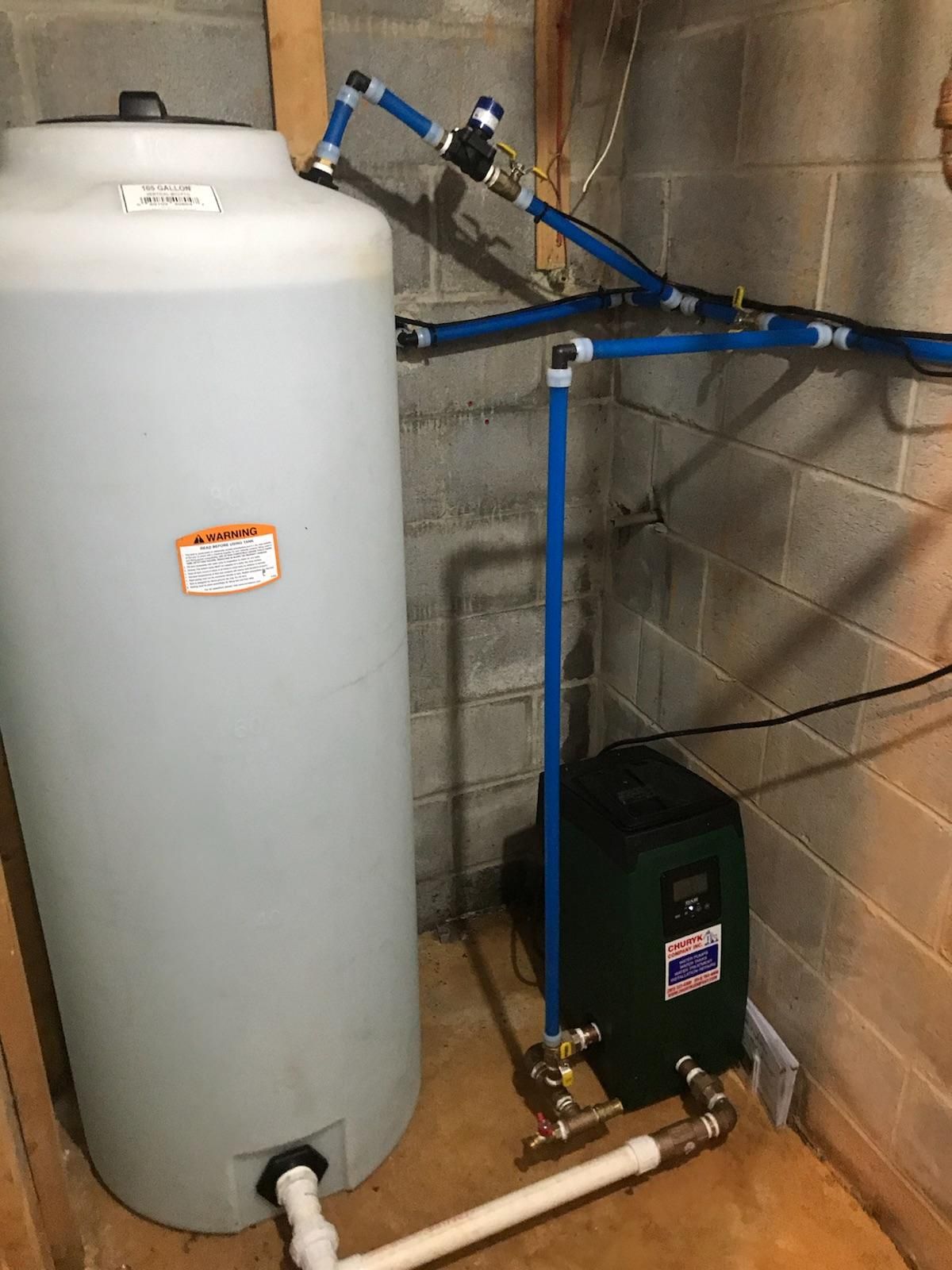 A water tank is sitting in a basement next to a brick wall.