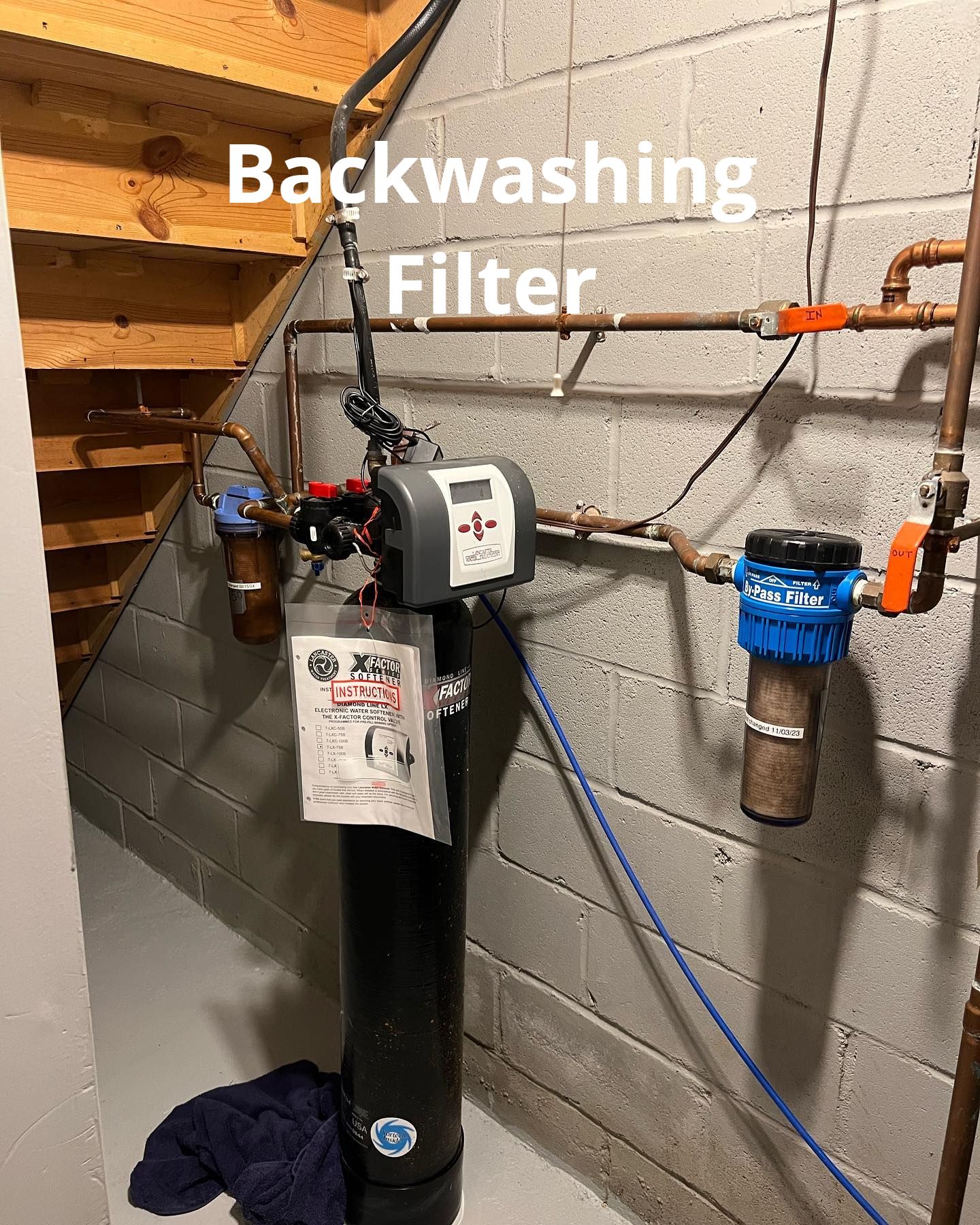 A backwashing filter is sitting in a basement next to a staircase.