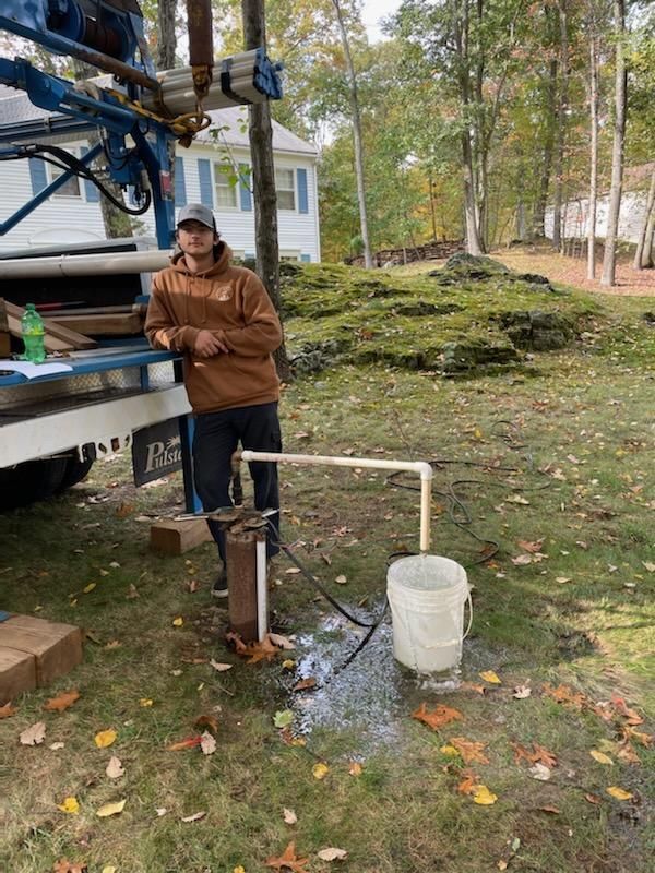 A man is standing next to a water pump in a yard.