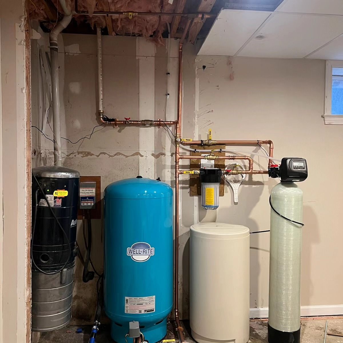 A room with a blue water tank , a white tank , and a water filter.