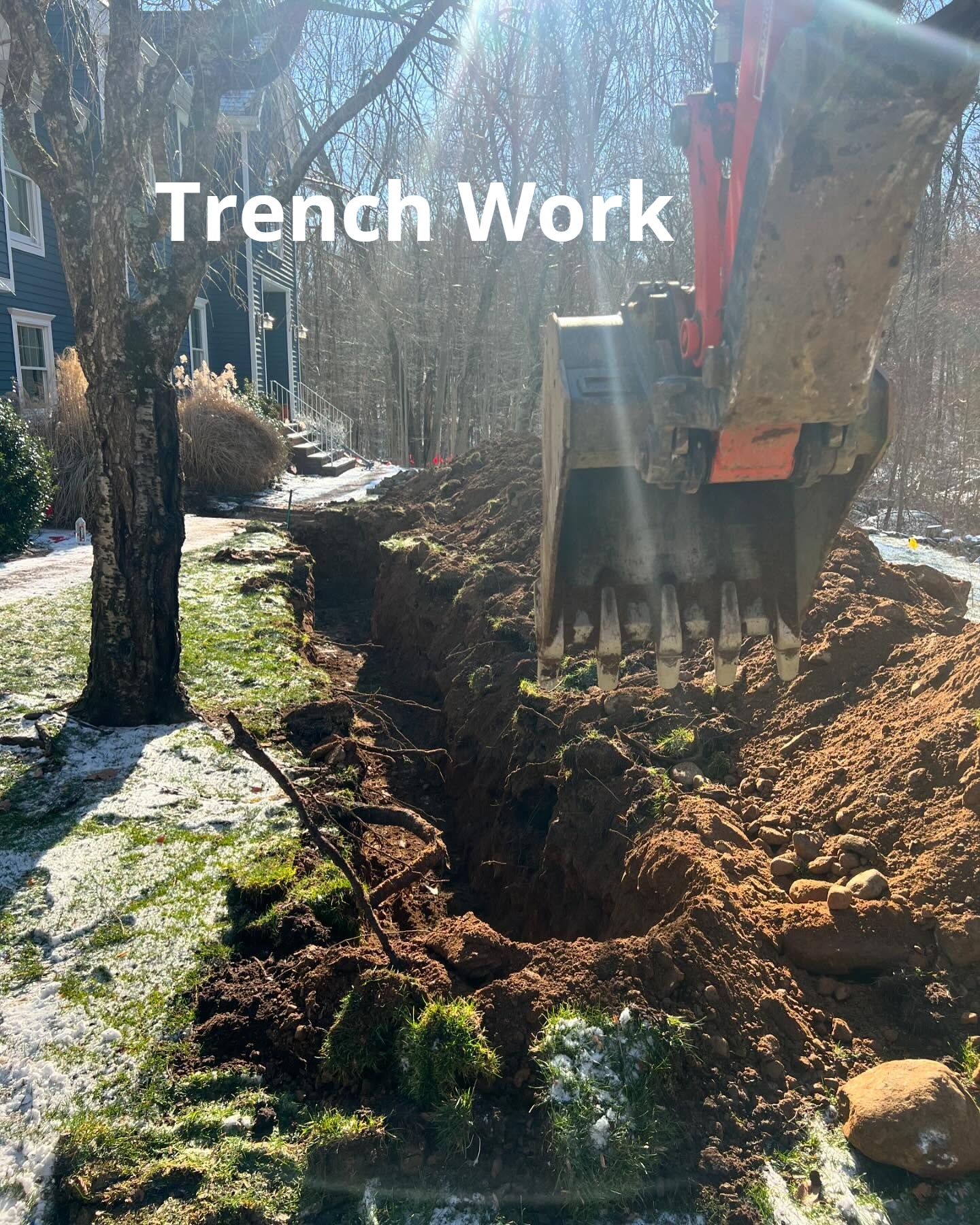 A large excavator is digging a trench in a yard.