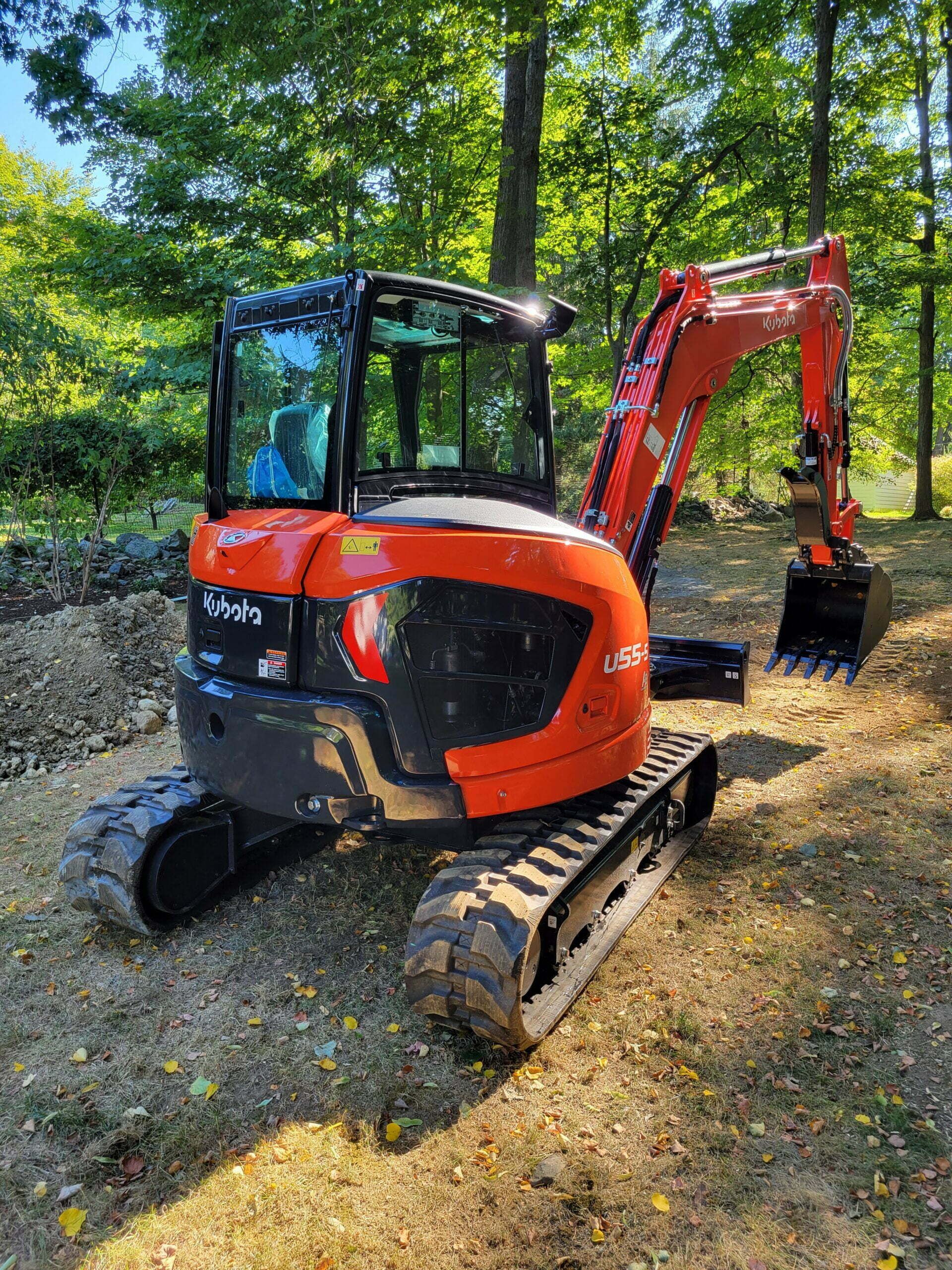 A small orange excavator is parked in the middle of a forest.