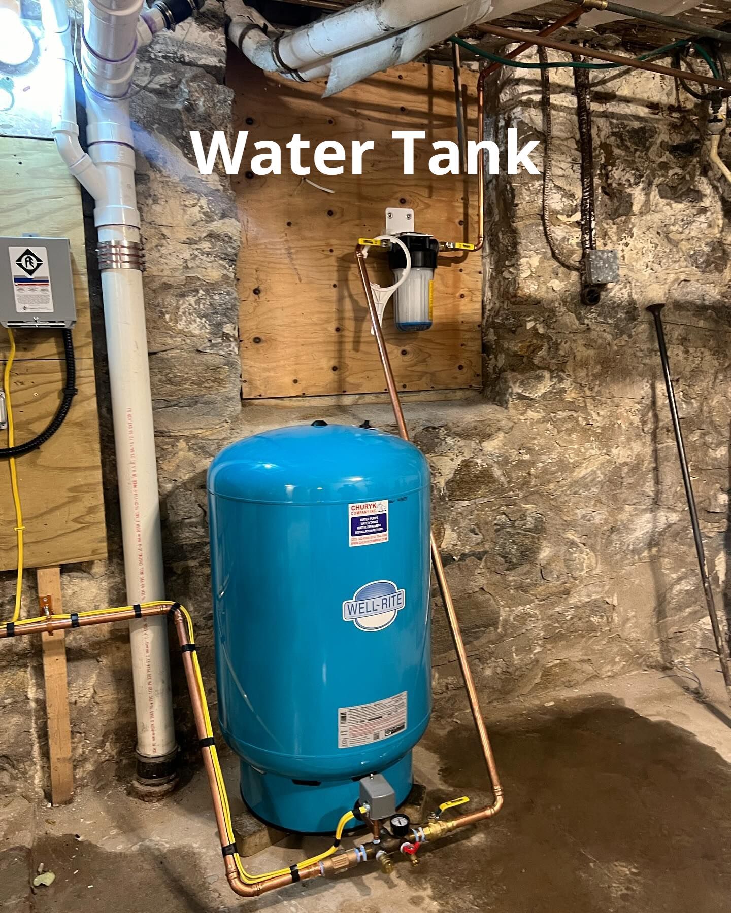A blue water tank is sitting in a basement next to a stone wall.