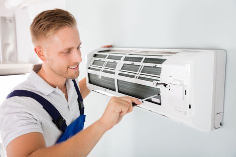 Technician cleaning a wall-mounted air conditioner with a tool