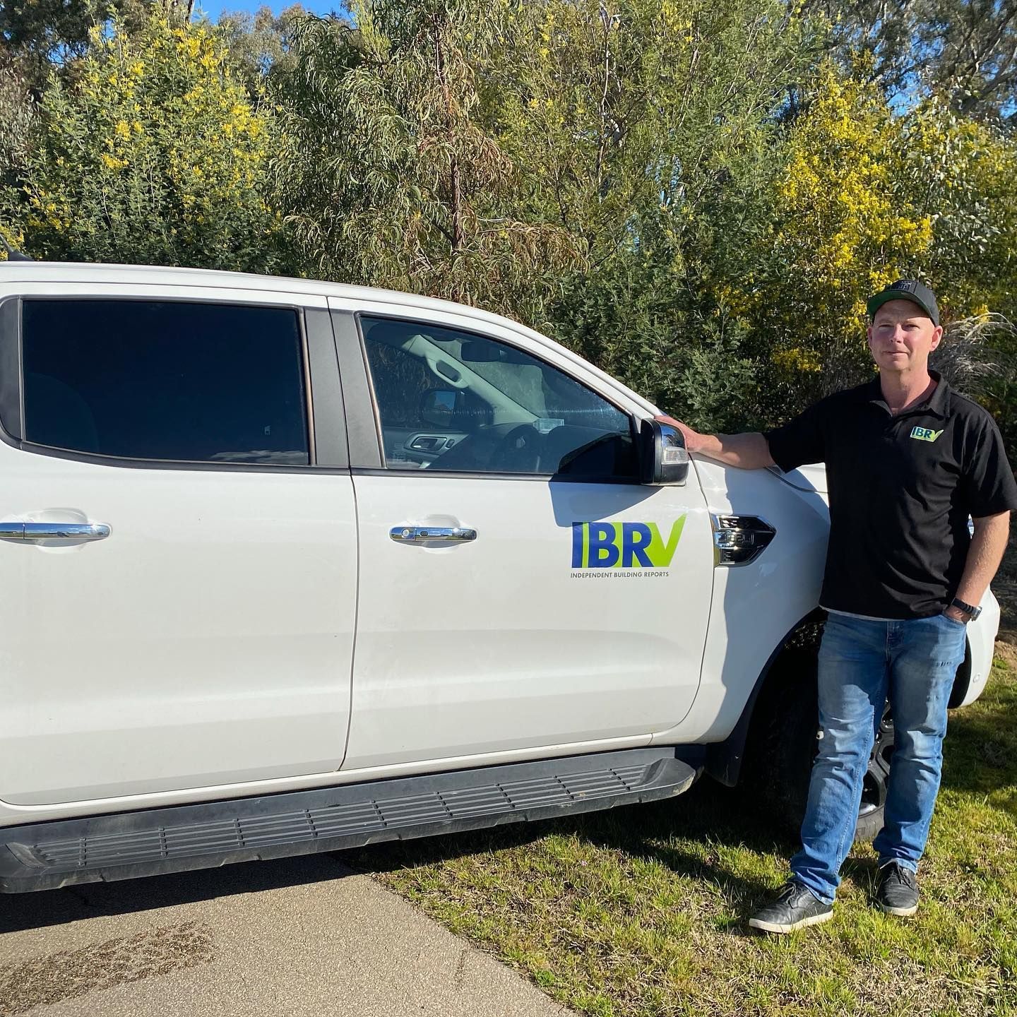 Man in black shirt and jeans stands next to white pickup truck with 