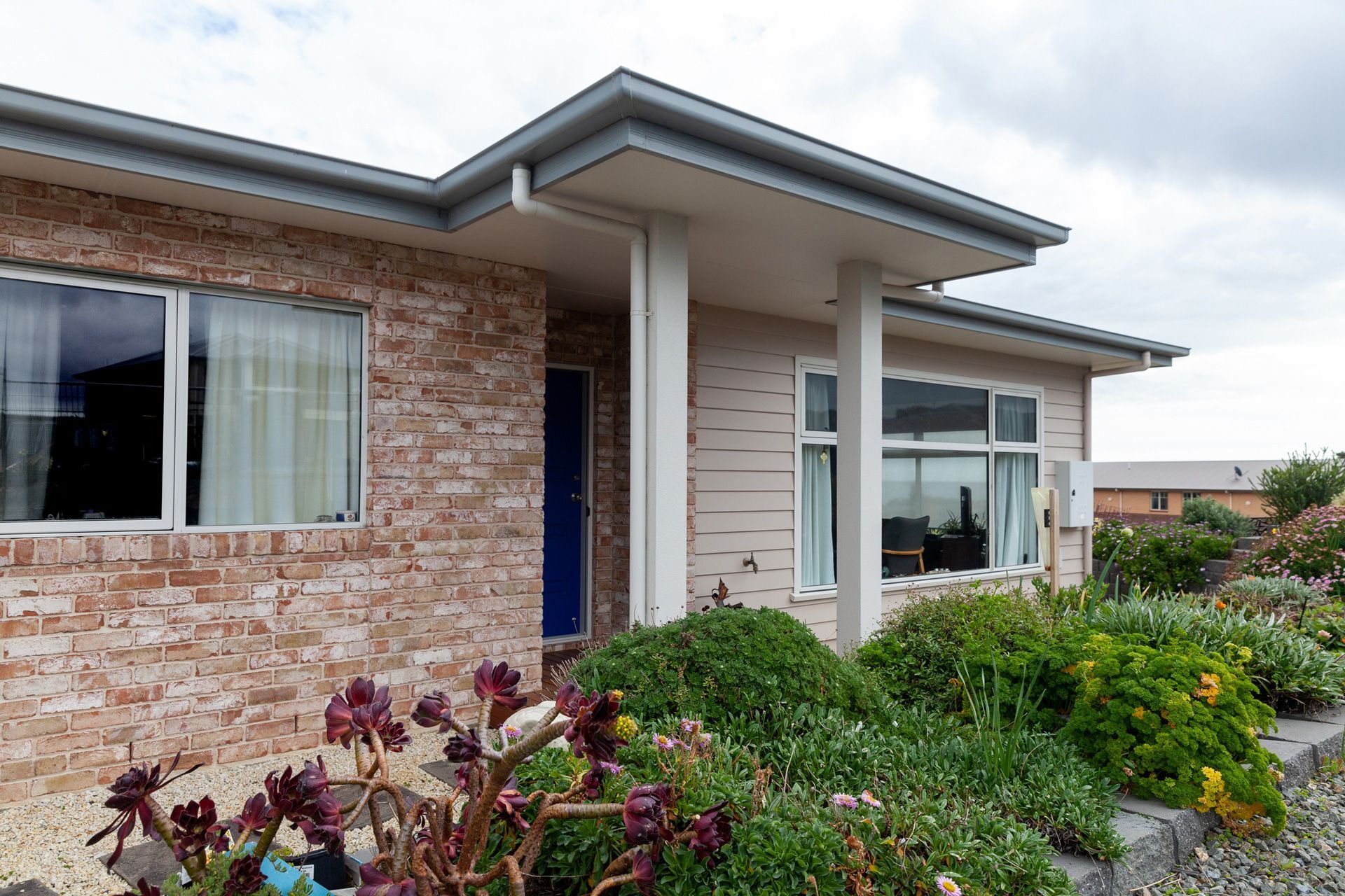 Brick house with a blue door, white trim, and garden. Overcast day.