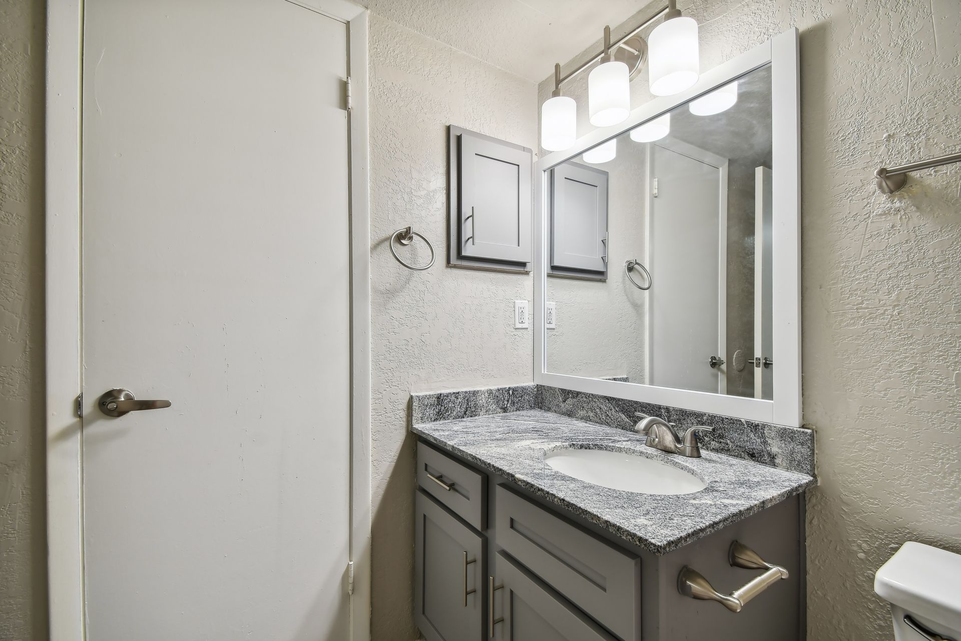 Bathroom with gray vanity, granite countertop, and white textured walls; mirror with overhead lighting at Timberlake in Altamonte Springs, FL.
