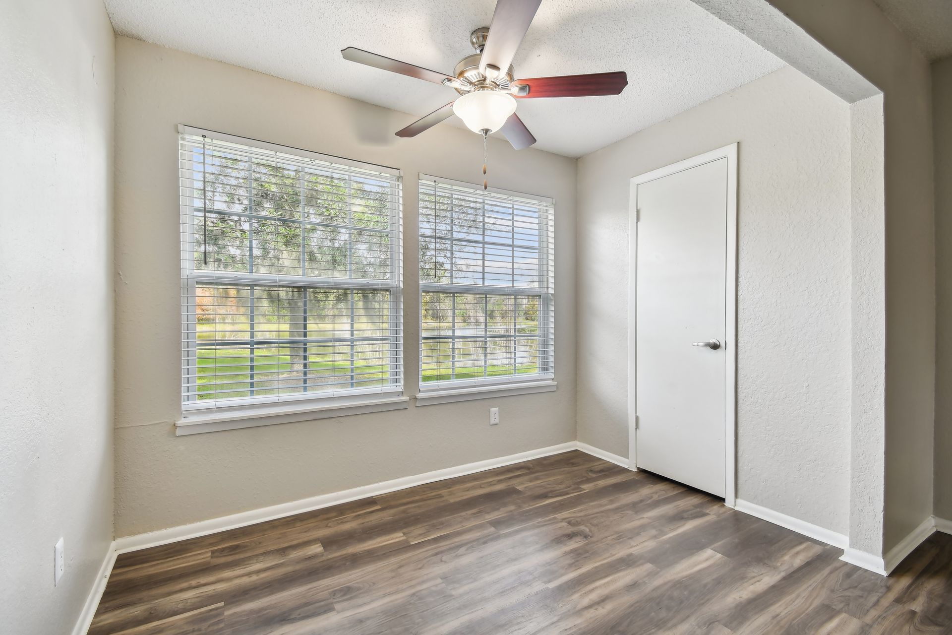 Bedroom with two windows, ceiling fan, and hardwood floors. White door on the right at Timberlake in Altamonte Springs, FL.