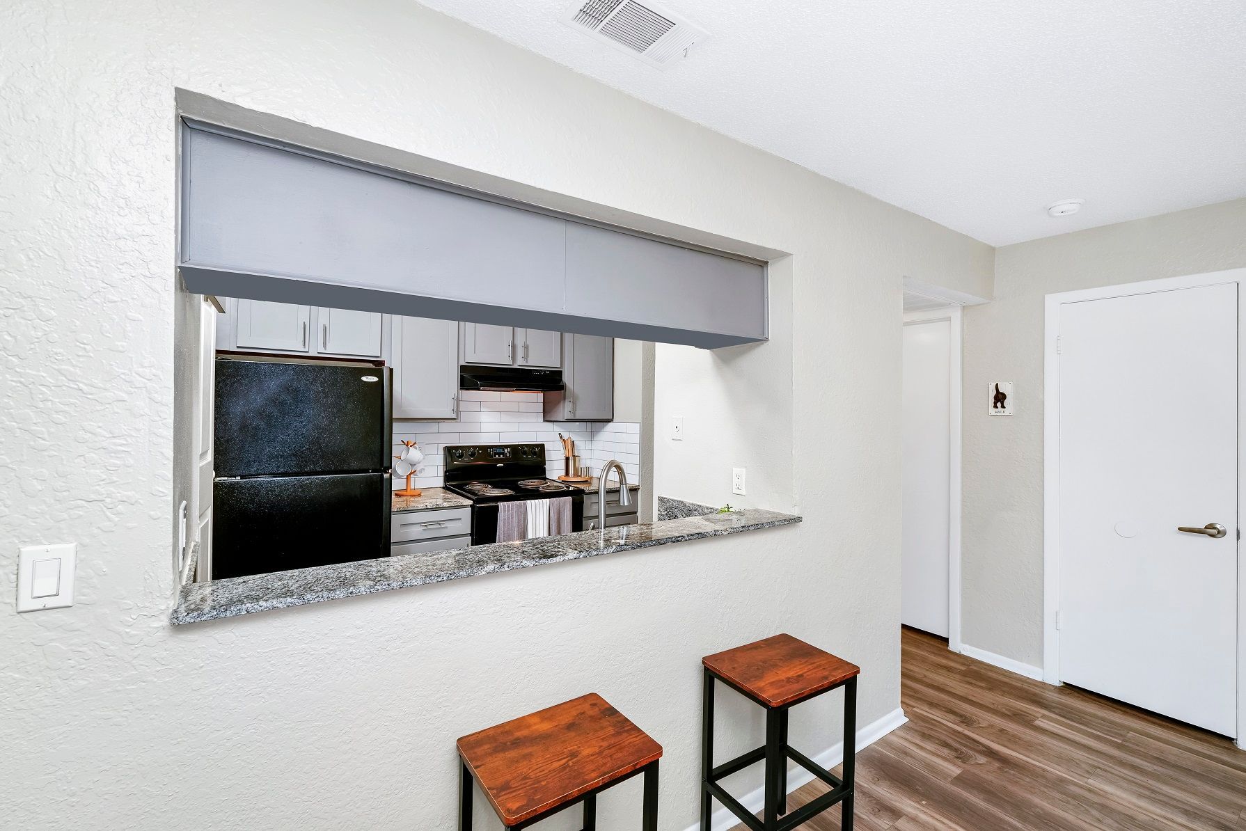 Kitchen pass-through with two stools. Black appliances, gray cabinets, and a white wall at Timberlake in Altamonte Springs, FL.