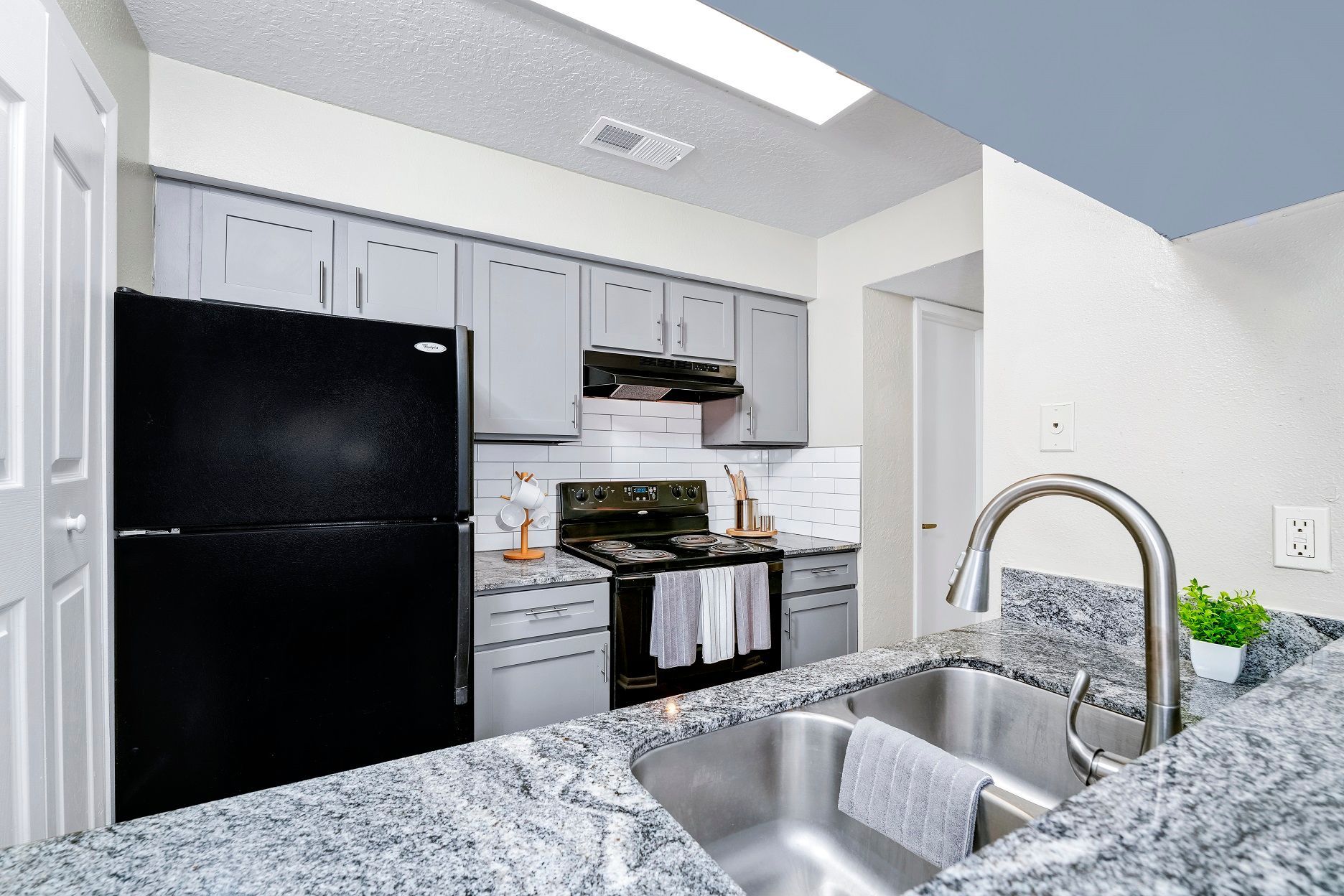 Kitchen with black refrigerator, gray cabinets, granite countertops, and stainless steel sink at Timberlake in Altamonte Springs, FL.