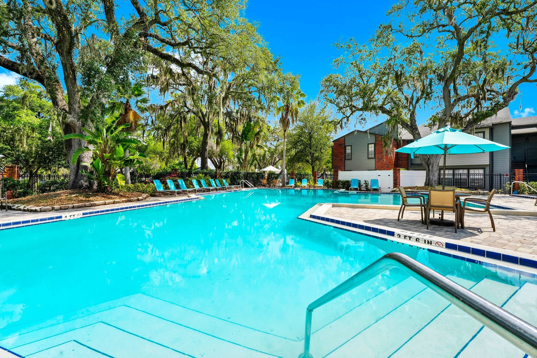 Swimming pool surrounded by trees and lounge chairs under a blue umbrella on a sunny day at Timberlake in Altamonte Springs, FL.