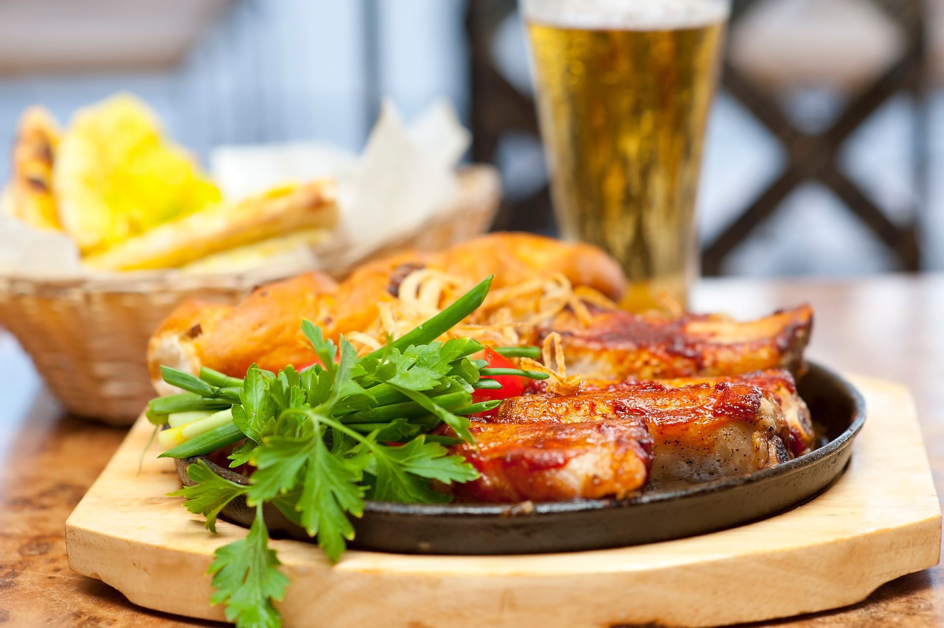 An overhead, close-up shot of an outdoor dining table featuring a plate of grilled fish topped with an herb mixture, served with a side of potato wedges in a small white bowl, a fresh garden salad with shredded carrots, and a lemon slice.