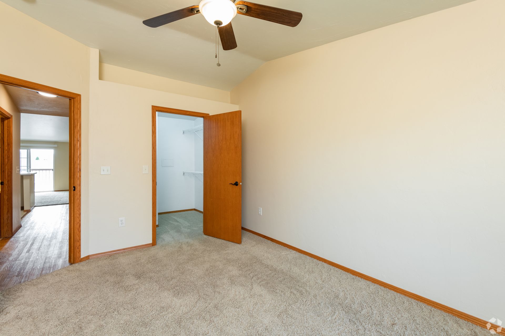 Empty bedroom with beige carpet, white walls, open closet, and ceiling fan