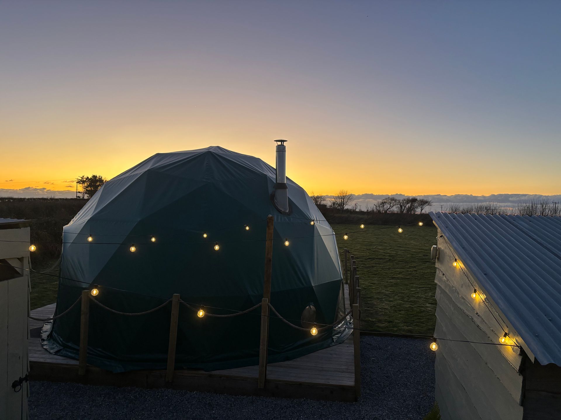 A dome tent with a chimney on top of it is lit up at sunset.