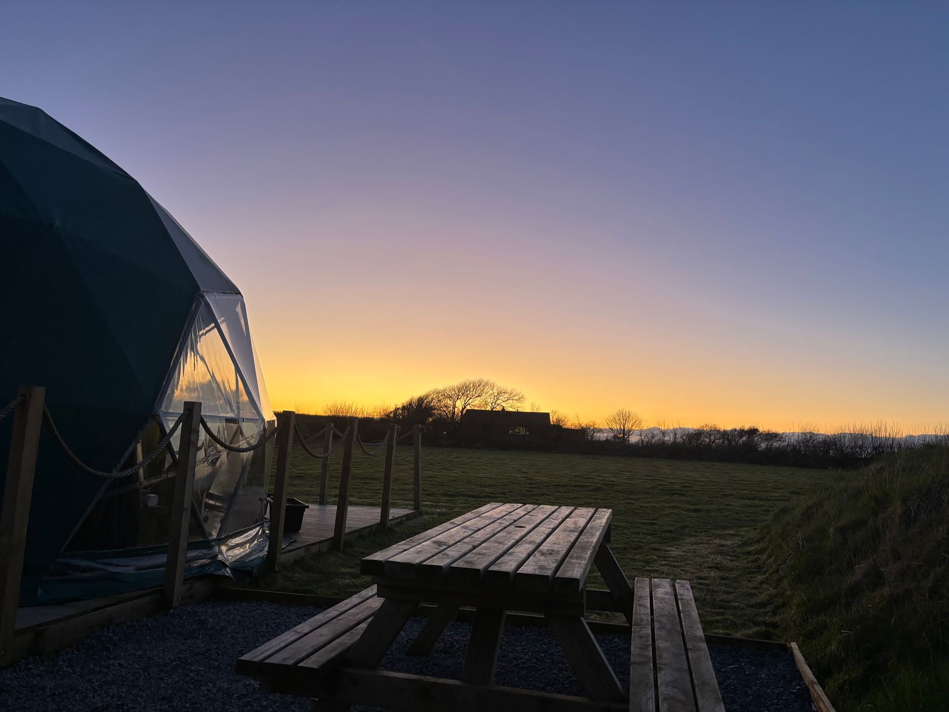 A picnic table in front of a tent at sunset.