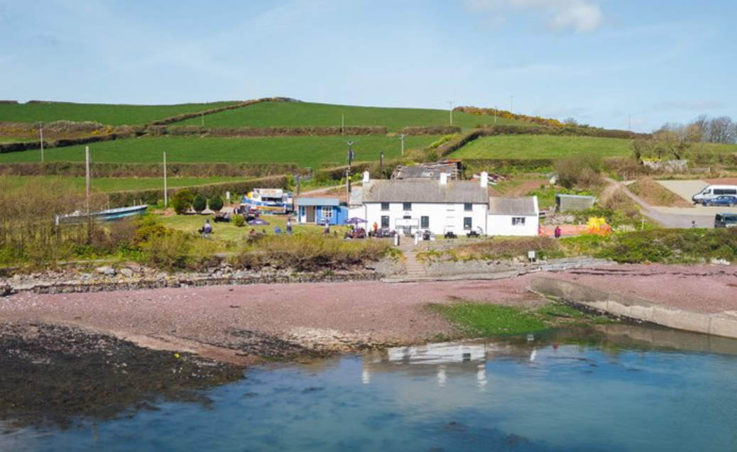 A white house is sitting on the shore of a body of water.