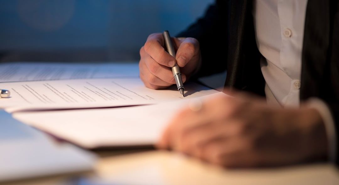 a man is writing on a piece of paper with a pen .