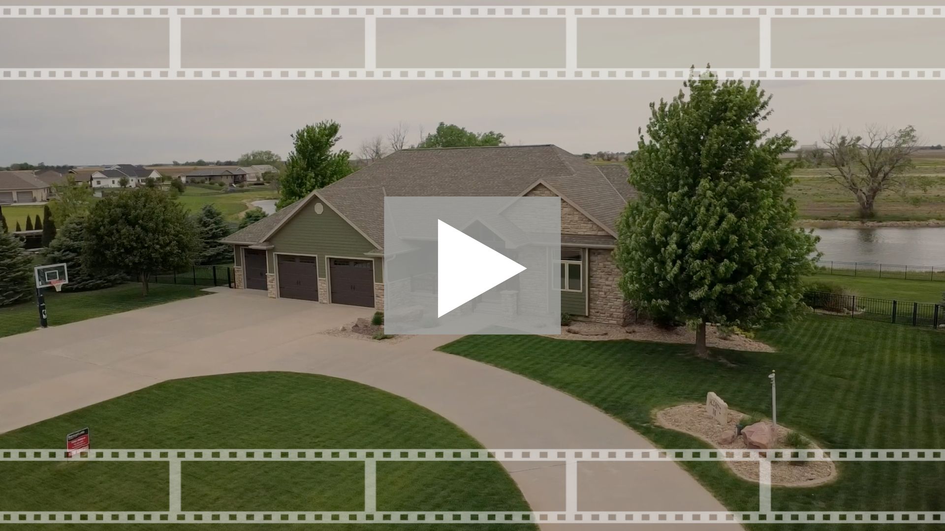 Aerial view of a suburban house with a curved driveway, green lawn, and large trees.
