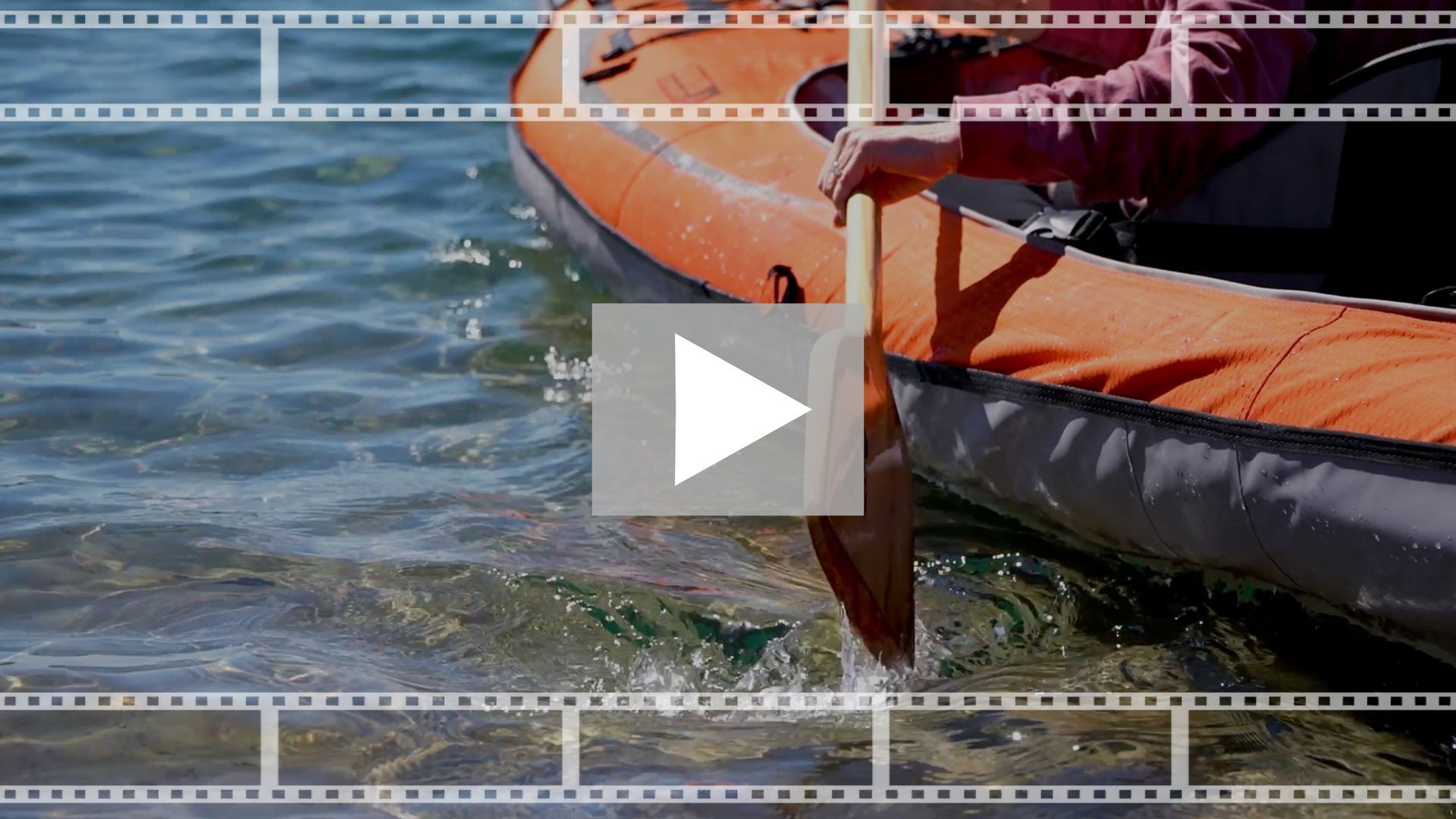 Orange kayak floating on rippling water with a paddle blade visible