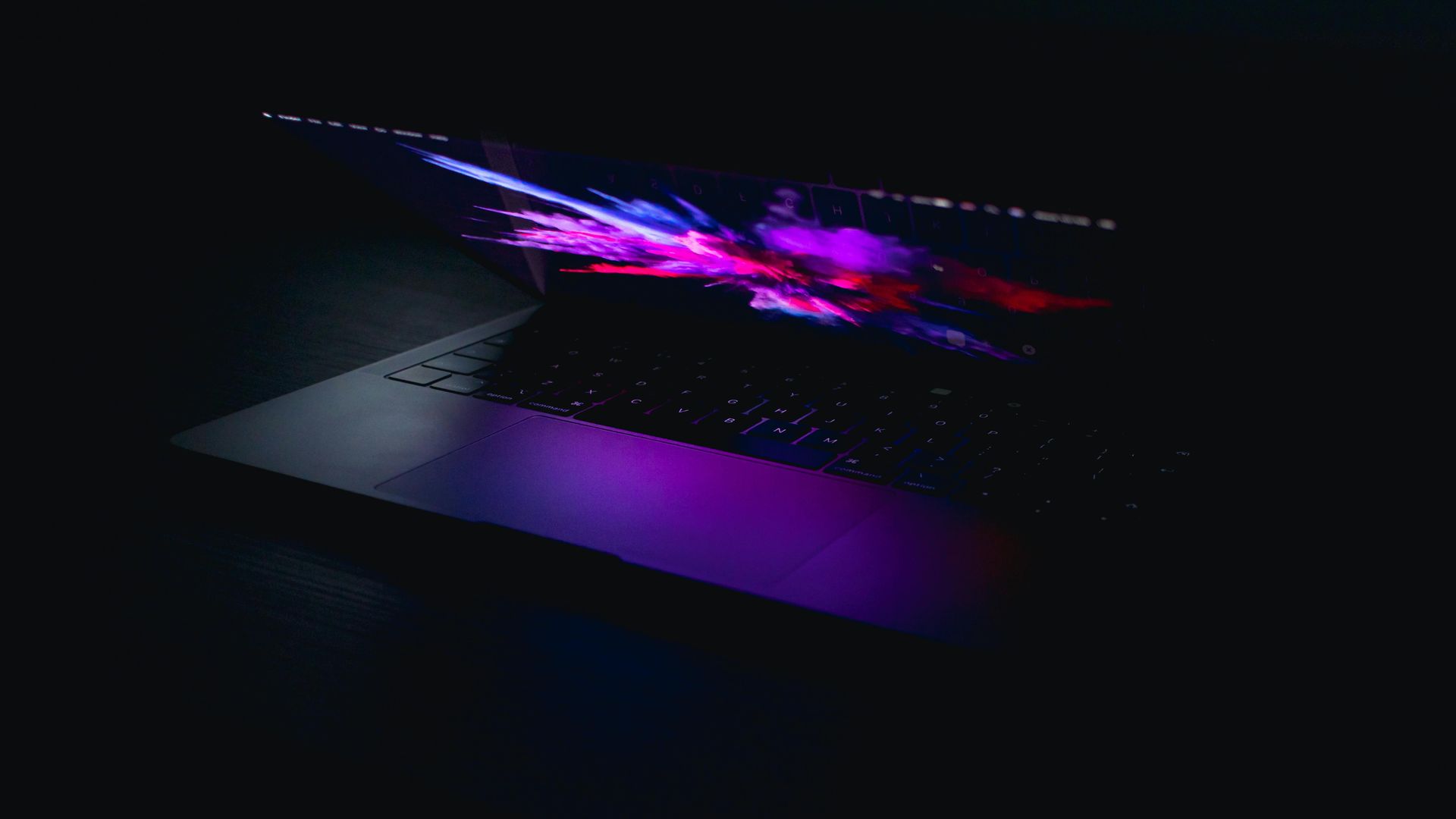 A laptop computer is sitting on a table in the dark with purple lights on it.