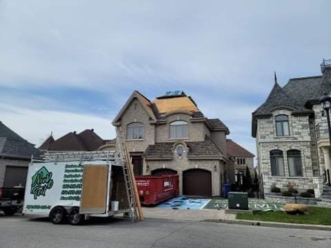 Une rue résidentielle avec une maison en cours de réparation de toiture, avec une remorque à benne basculante, un conteneur à déchets rouge et une échelle.