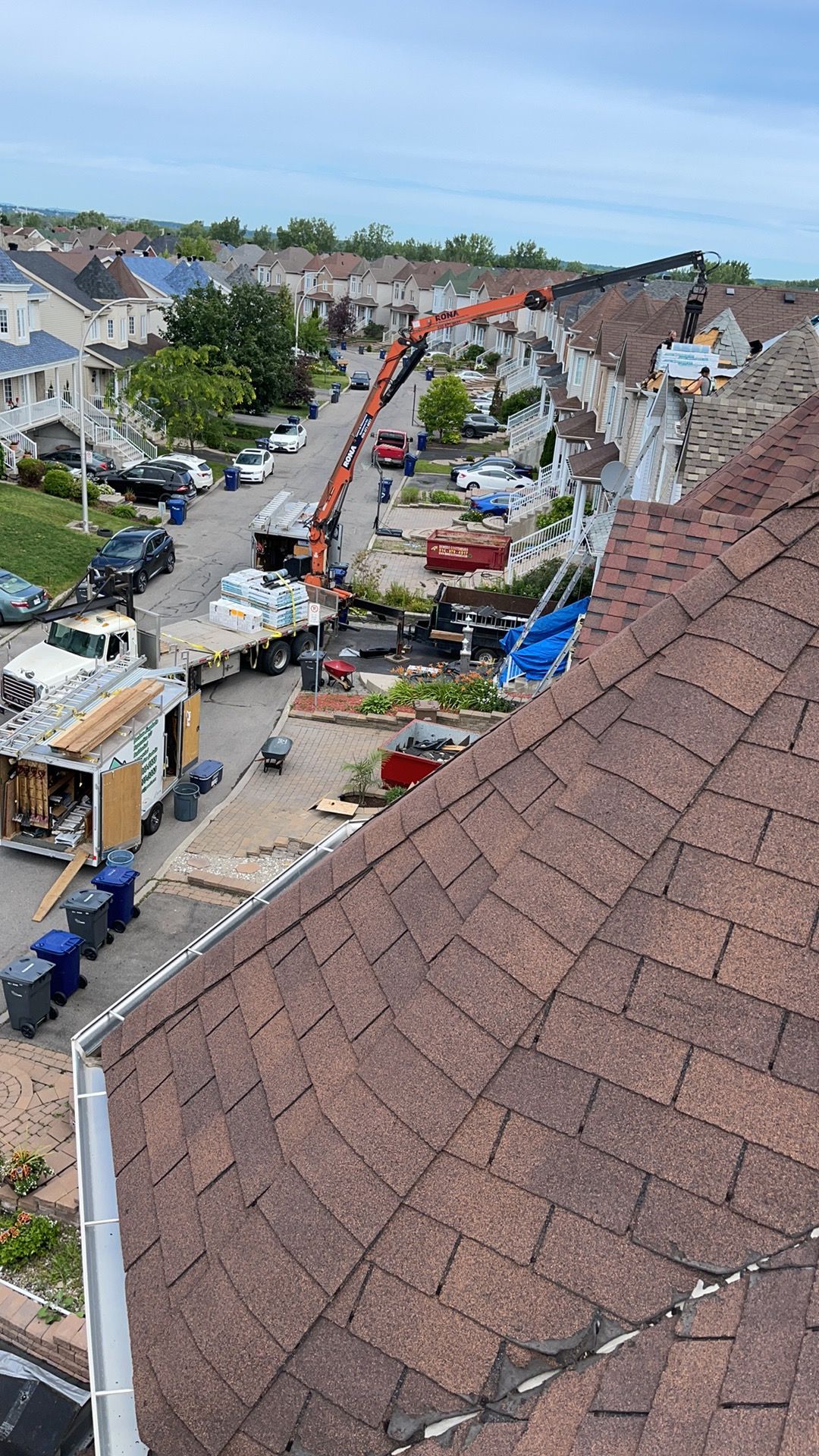 Une grue de chantier soulève des matériaux sur le toit d'une maison dans un quartier résidentiel de banlieue.